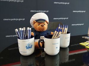 Zdjęcie w kolorze przedstawia fragment  stanowiska promocyjnego policji z maskotką - misiem policjantem i innymi materiałami promocyjnymi.