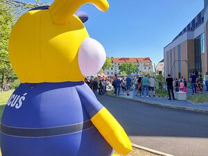 Zdjęcie w kolorze przedstawia na pierwszym planie po lewej stronie dużą dmuchaną maskotkę opolskiej policji - królika policusia po prawej stronie tłum ludzi przy stoiskach wyeksponowanych podczas wydarzenia przy Centrum Sportu i rekreacji 5 Poziom w Oleśnie.