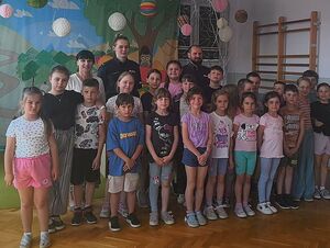 Zdjęcie w kolorze przedstawia spotkanie dzieci z policjantami w sali gimnastycznej.