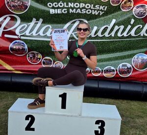 Zdjecie przedstawia kobietę w stroju sportowym siedzącą na podium.