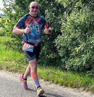 Zdjęcie w kolorze przedstawia policjanta w stroju sportowym biegnacego drogą asfaltową.
