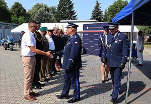 Zdjęcie w kolorze przedstawia pełniącego obowiązki Komendanta Powiatowego Policji w Oleśnie oraz Zastępcę Komendanta Wojewódzkiego Policji w Opolu podczas wręczania podarunków wyróżnionym gościom.