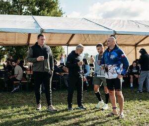Zdjęcie w kolorze przedstawia czterech mężczyzn stojących na trawniku za nimi duży namiot okolicznościowy