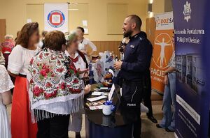 Zdjęcie w kolorze przedstawia seniorów w strojach ludowych przed stoiskiem policyjnym