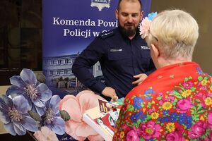 Zdjęcie w kolorze przedstawia seniorów w strojach ludowych przed stoiskiem policyjnym