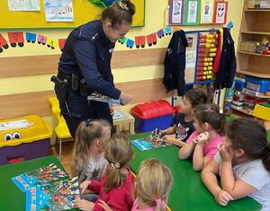 Zdjęcie przedstawia grupę dzieci pośród których policjantka wręcza książki " pierwszaki"