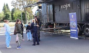 zdjęcie przedstawia policjantkę stojącą z grupą osób, w tle stoi czarna ciężarówka