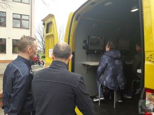 Policjant i egzaminator WORD Opole stoją przy mobilnym centrum egzaminacyjnym, uczniowie piszą próbny test na prawo jazdy kategorii AM