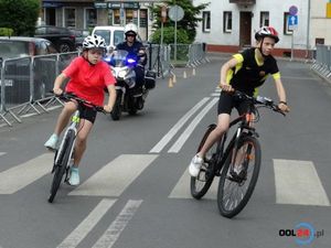 Młodzi kolarze na trasie wyścigu za nimi jedzie policjant na motocyklu