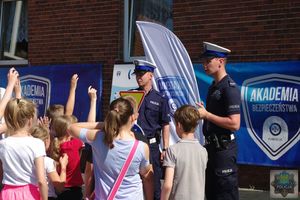 Policjanci ruchu drogowego zadają dzieciom pytania dotyczące bezpiecznego poruszania się rowerem. Dzieci podnoszą ręce zgłaszając się do odpowiedzi.