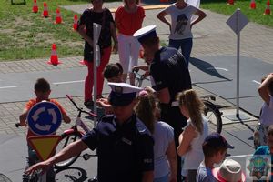 Policjanci drogówki udzielają wskazówek dzieciom na rowerach jak bezpiecznie poruszać się rowerem po miasteczku ruchu drogowego.