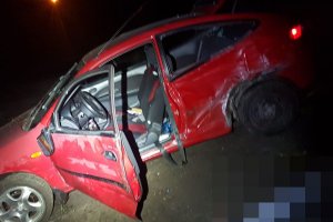 Czerwony, uszkodzony samochód osobowy stoi w polu, w nocy.