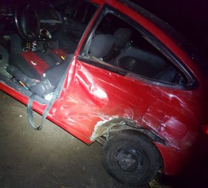 Bok czerwonego, uszkodzonego samochodu osobowego, który stoi w polu, w nocy.