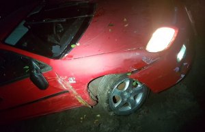 Uszkodzony czerwony samochód osobowy stoi w nocy z włączonymi światłami mijania.