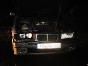 Spalone BMW stoi w nocy na poboczu drogi.
