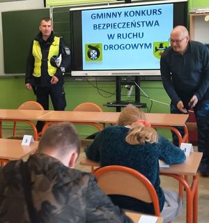 Policjant w mundurze stoi przy włączonej tablicy multimedialnej.
