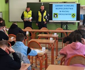 Dwóch policjantów w mundurach stoi przy tablicy w klasie szkolnej.