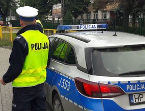 Policjanci drogówki w mundurach stoją przy oznakowanym radiowozie.