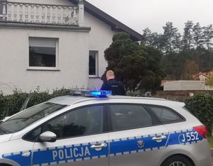 Radiowóz policyjny stoi przy domku jednorodzinnym.