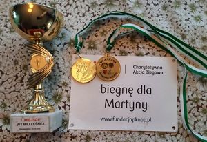 Puchar, dwa medale i kartka z napisem Biegnę dla Martynki.