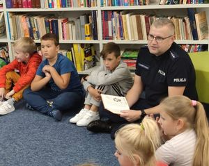 Policjant w mundurze siedzi z dziećmi na dywanie i czyta im bajki.
