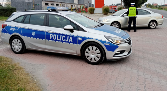 radiowóz, samochód i kontrolujący kierowce policjant