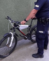 Mężczyzna umundurowany w policyjny mundur stoi obok roweru górskiego.