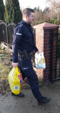 Umundurowany policjant niesie w rękach dwie torby karmy dla zwierząt.