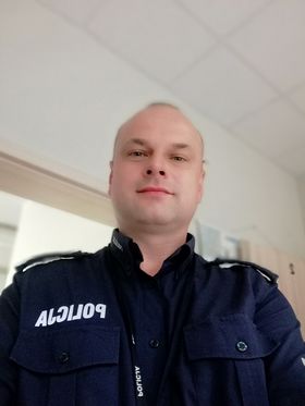 Mężczyzna z ogoloną głową stoi w policyjnym mundurze.