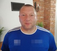 Łysy mężczyzna stoi na tle ceglanej ściany.