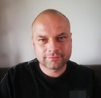 Łysy mężczyzna pozuje w czarnym swetrze.