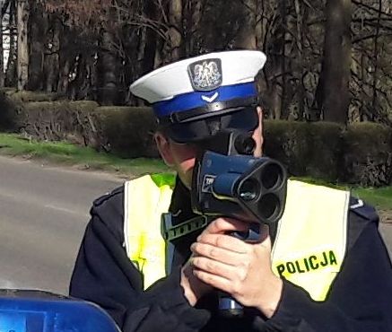 Policjant w mundurze i białej czapce mierzy prędkość kierowcom za pomocą radaru.