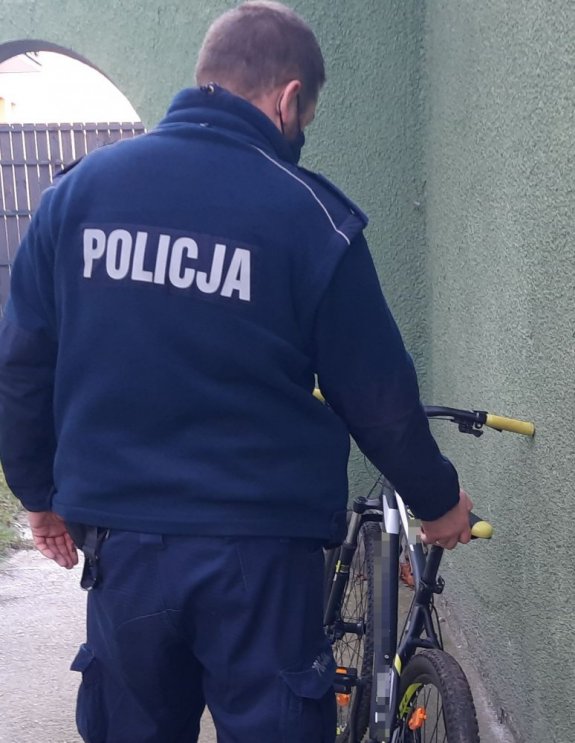 Policjant w mundurze stoi przy rowerze górskim i trzyma go za siodło.