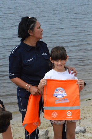 policjantka stojąca z dzieckiem, trzymającym plecak z napisem kręci mnie bezpieczeństwo nad wodą