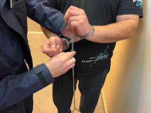policjant zakłada kajdanki zespolone na ręce trzymane z przodu zatrzymanemu