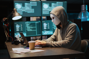 osoba w masce siedząca przed laptopem i pisząca na klawiaturze