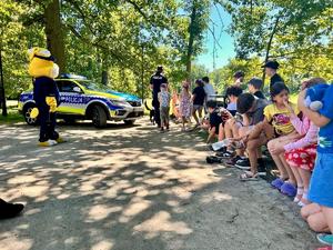 grupa dzieci słuchająca prelekcji policjantki , widoczna maskotka policji policuś
