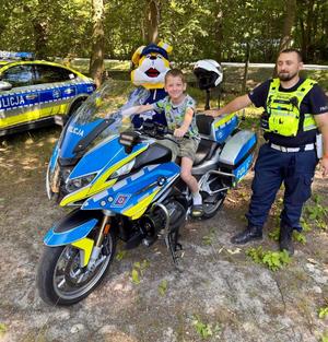 policjant ruchu drogowego stoi przy służbowym motocyklu, na motocyklu dziecko pozuje do zdjęcia