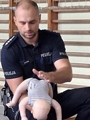 policjant ilustrujący jak ratować niemowlę w razi zadławienia