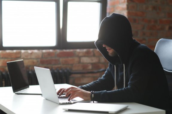 mężczyzna w naciągniętym na głowę kapturem siedzący przed otwartym laptopem