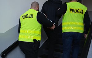 2 policjanci prowadzą zatrzymanego mężczyznę korytarzami
