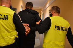 2 policjanci prowadzą zatrzymanego mężczyznę korytarzami