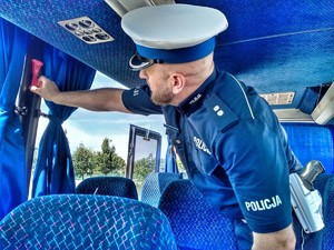 Zdjęcie przedstawia policjanta kontrolującego wyposażenie autobusu.