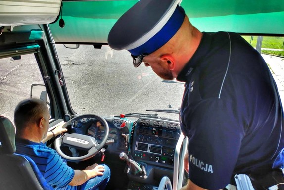 Zdjęcie przedstawia policjanta, sprawdzającego układ kierownicy autokaru.