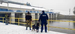 policjant, strażnik rybacki i pies służbowy stoją obok siebie przy rzece