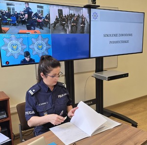 Zdjęcie przedstawia policjantkę, za nią stoją monitory.