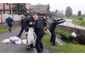 Zdjęcie przedstawia policjantów przerzucający worki nad rzeką.