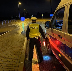 Zdjęcie przedstawia policjanta ruchu drogowego nocą, w tle zalana droga.