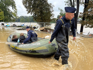 policjant w woderach ciągnący ponton z ewakuowanymi osobami