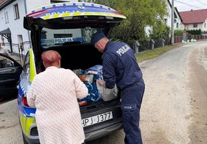 Policjant przekazuje paczkę potrzebującej kobiecie.